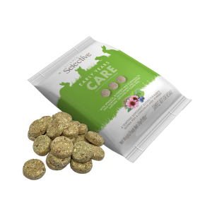 A 25g sachet of Science Selective Early Years Care supplements shown next to a small pile of the round, compressed supplement discs. The white and green packaging features silhouettes of small animals and highlights key ingredients like spinach, blueberry, and echinacea. The discs are light brown with visible herbal flecks, designed for rabbits, guinea pigs, and chinchillas aged 10 weeks and over.